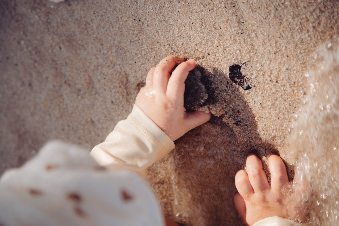 Barns hender utforsker en kongle i våt sand ved vannkanten